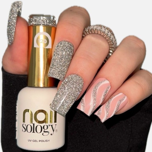 Clavier lakier hybrydowy z efektem Flash Nailsology "Silver Divine". Szklana buteleczka, w białym kolorze ze złotą nakrętką i elementami na etykiecie. Trzymana przez dłoń ze stylizacją wykonaną tym kolorem.