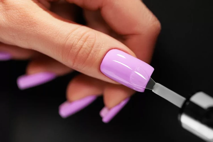Victoria Vynn top hybrydowy "It" no wipe 8 ml. Stylizacja przedstawia błysk topu na tle jasno-fioletowego lakieru. Manicure, długie paznokcie w kształcie kwadratu.