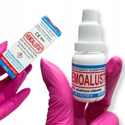 Dłoń w różowej rękawiczce trzymająca płyn hemostatyczny tamujący krwawienie do zacięć skórek 10 ml wraz z kartonikiem w który jest zapakowany.