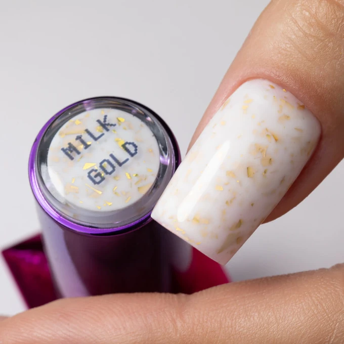 Pomalowany długi paznokieć kauczukową bazą Molly Lac ze złotymi płatkami flakes rubber base milk &amp; gold. HEMA FREE. Szklana buteleczka.